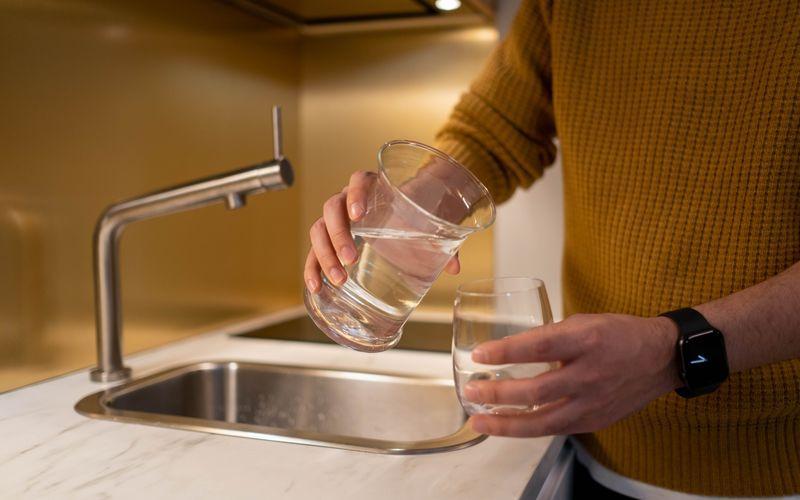 hand pouring clean filtered water into a clear drinking glass
