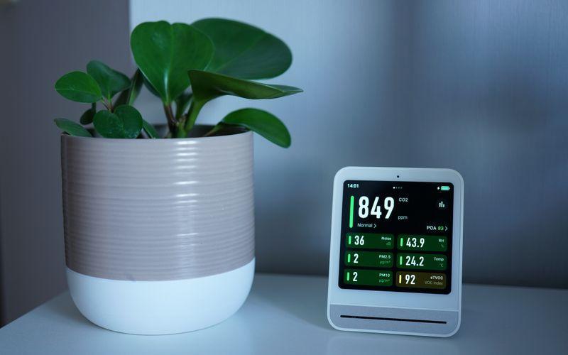 indoor air quality monitor showing carbon dioxide readings beside a green plant